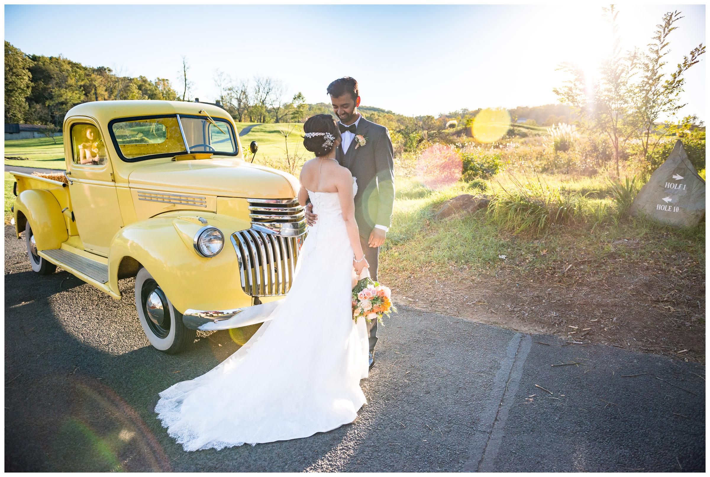 Portrait of bride and groom with vintage yellow truck during wedding at Stoneleigh Golf Club in Round Hill, Virginia.