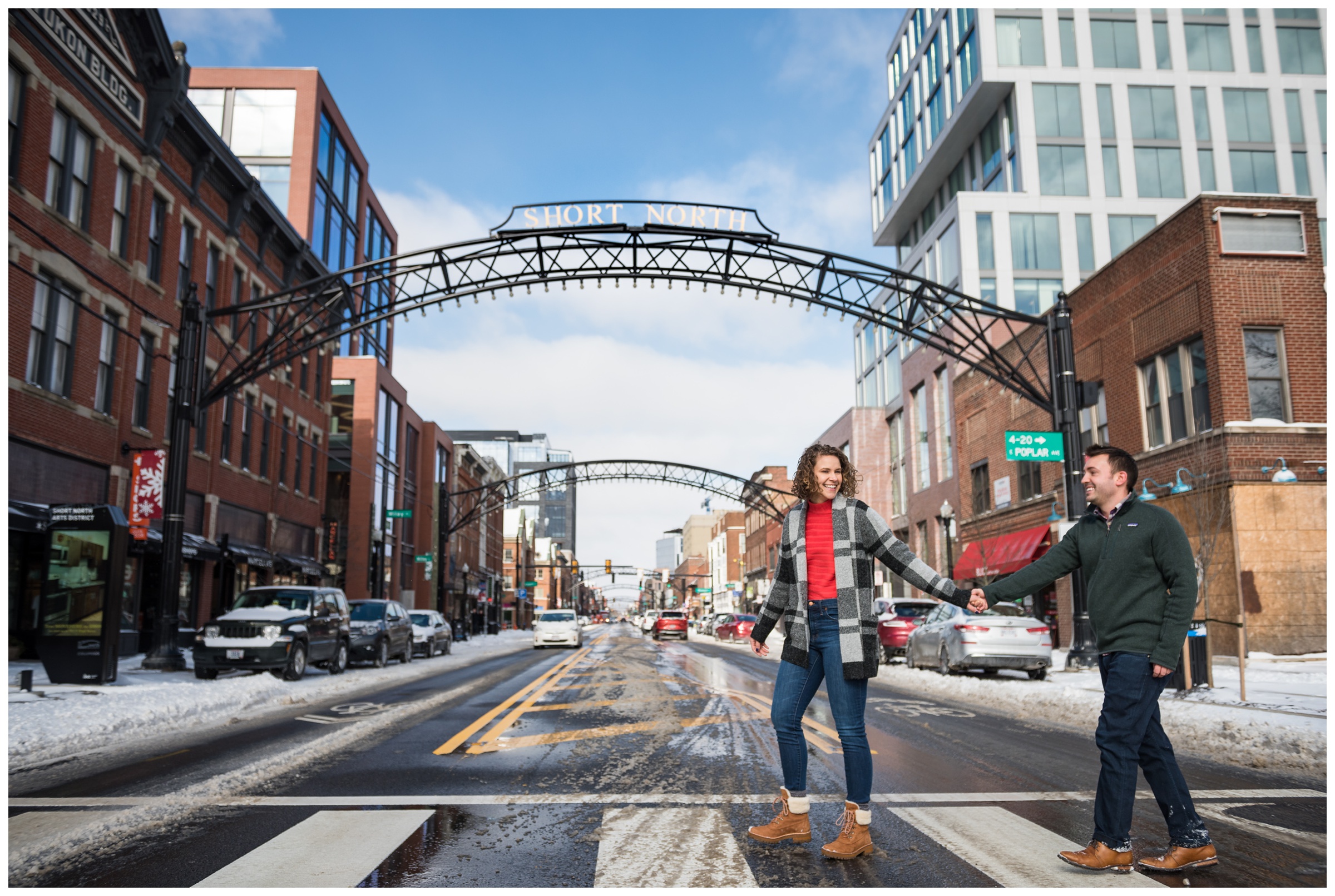 engaged couple walking under arches in the Short North neighborhood of Columbus, Ohio during snowy winter engagement session