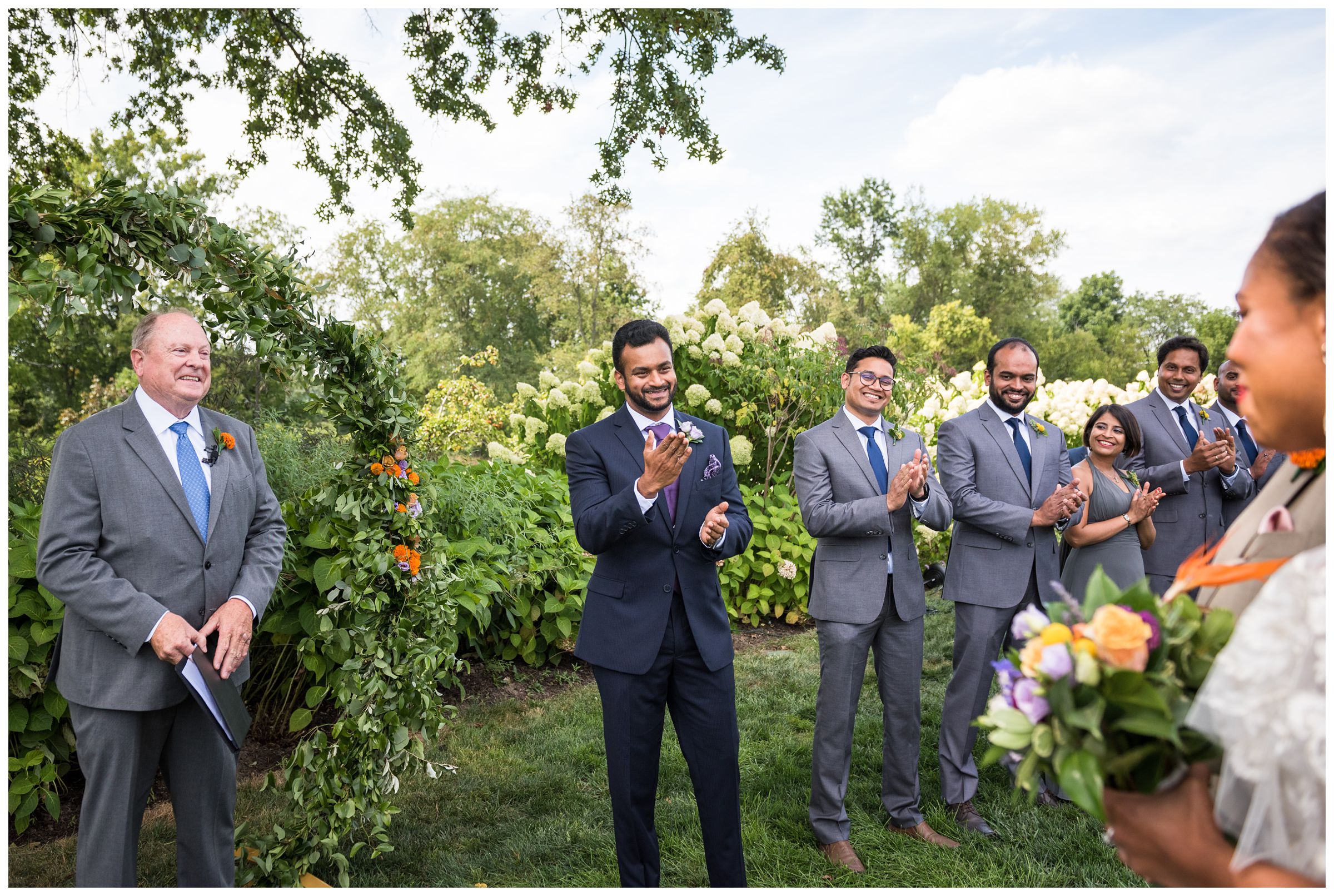 Indian groom waiting as black bride walks down aisle with father during summer Jorgensen Farms wedding