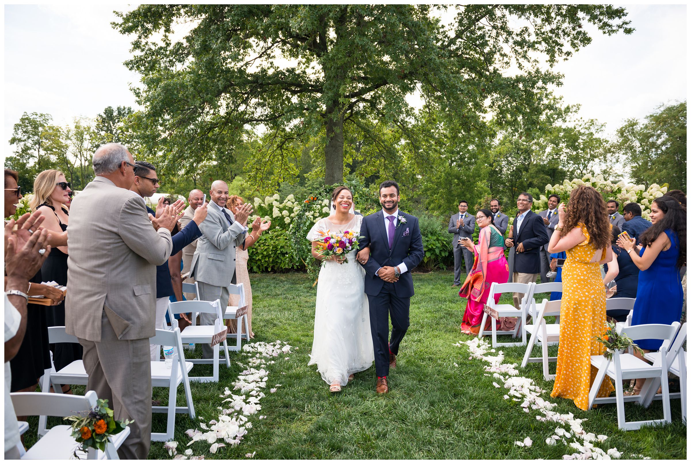 bride and groom exit wedding ceremony after colorful summer Indian wedding at Jorgensen Farms