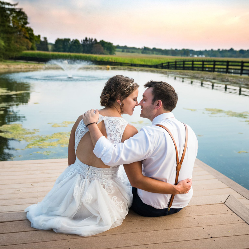 bride and groom sitting on a dock by a pond at sunset during a barn wedding reception on their family farm in Lancaster Ohio