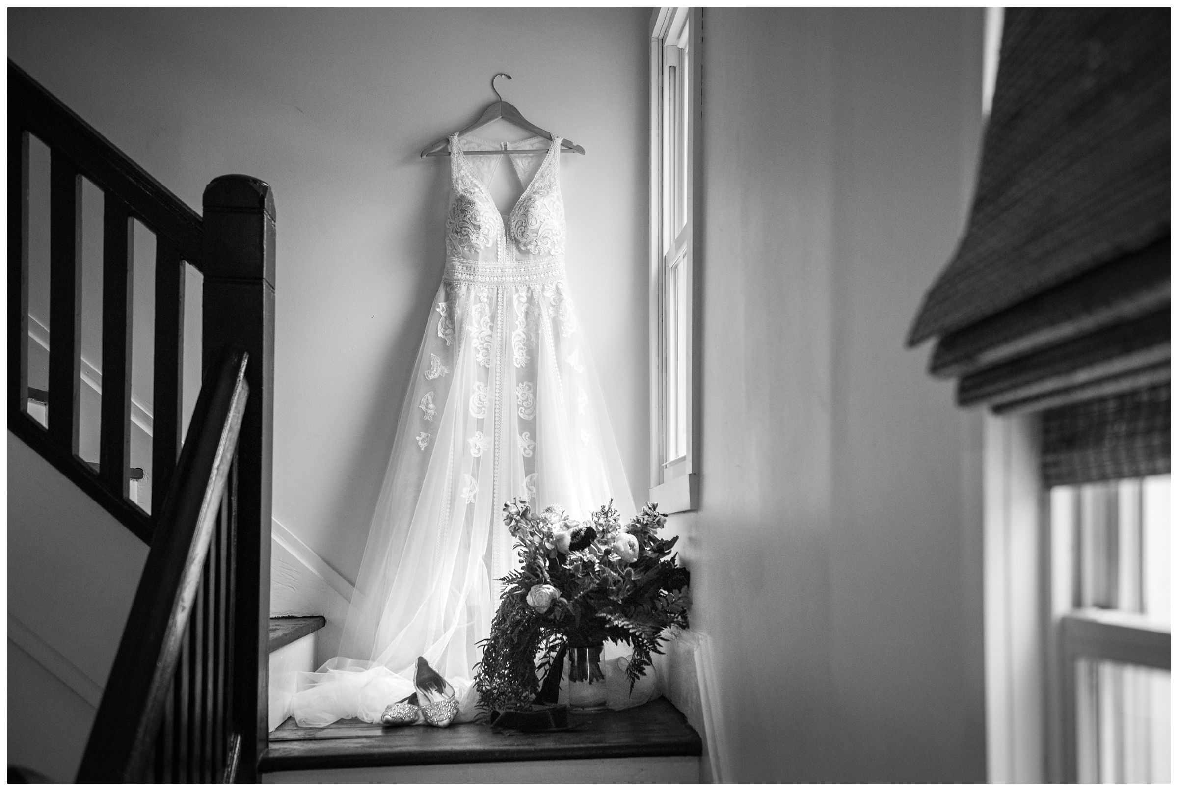 lace a-line wedding dress hanging on stairway by window with bouquet and shoes