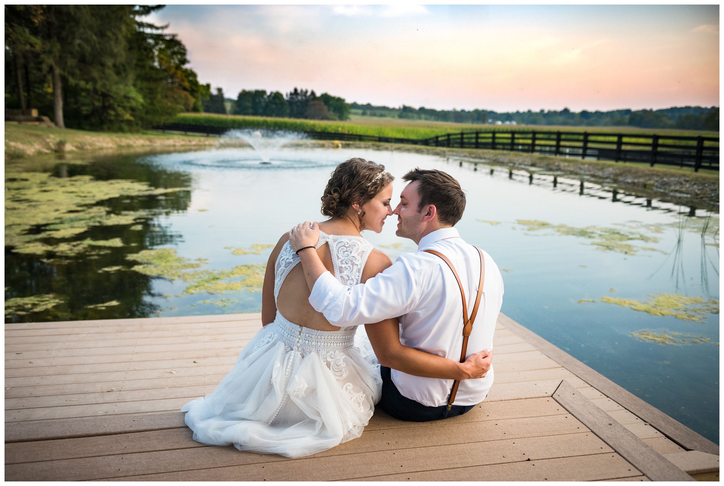 bride and groom sitting on dock by pond at sunset during rustic Lancaster barn wedding captured by Ohio wedding photographer