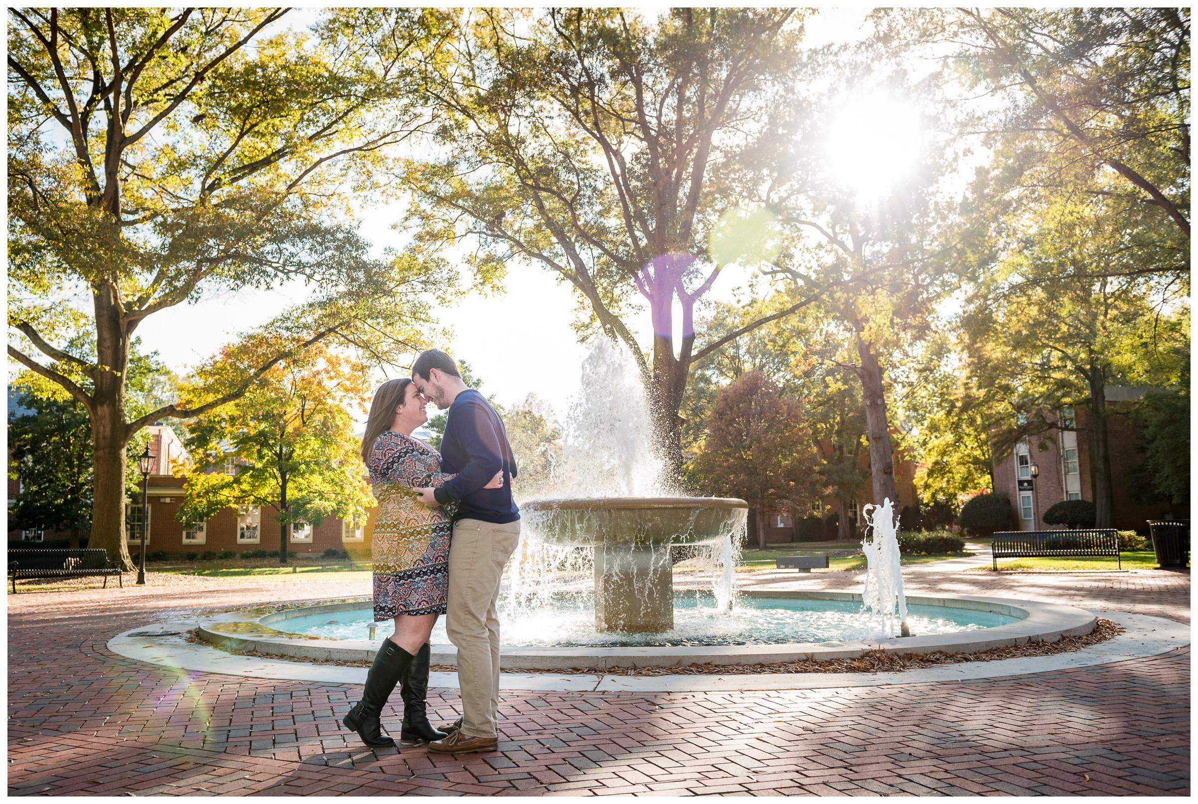 Engaged couple embracing near fountain with sunflare