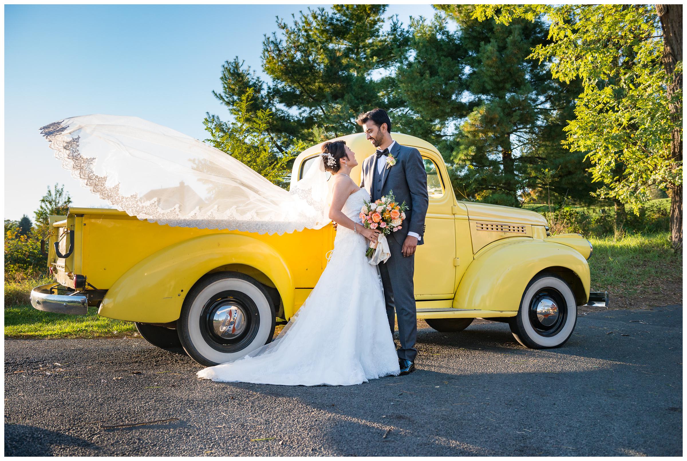 bride and groom with flowing veil and vintage yellow truck