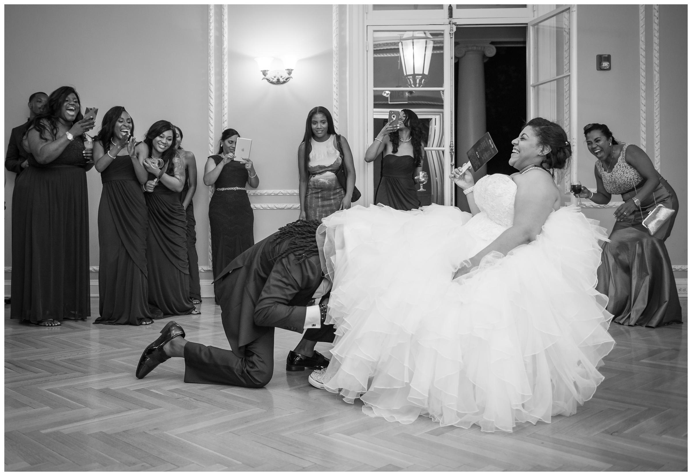 groom retrieving garter while guests laugh