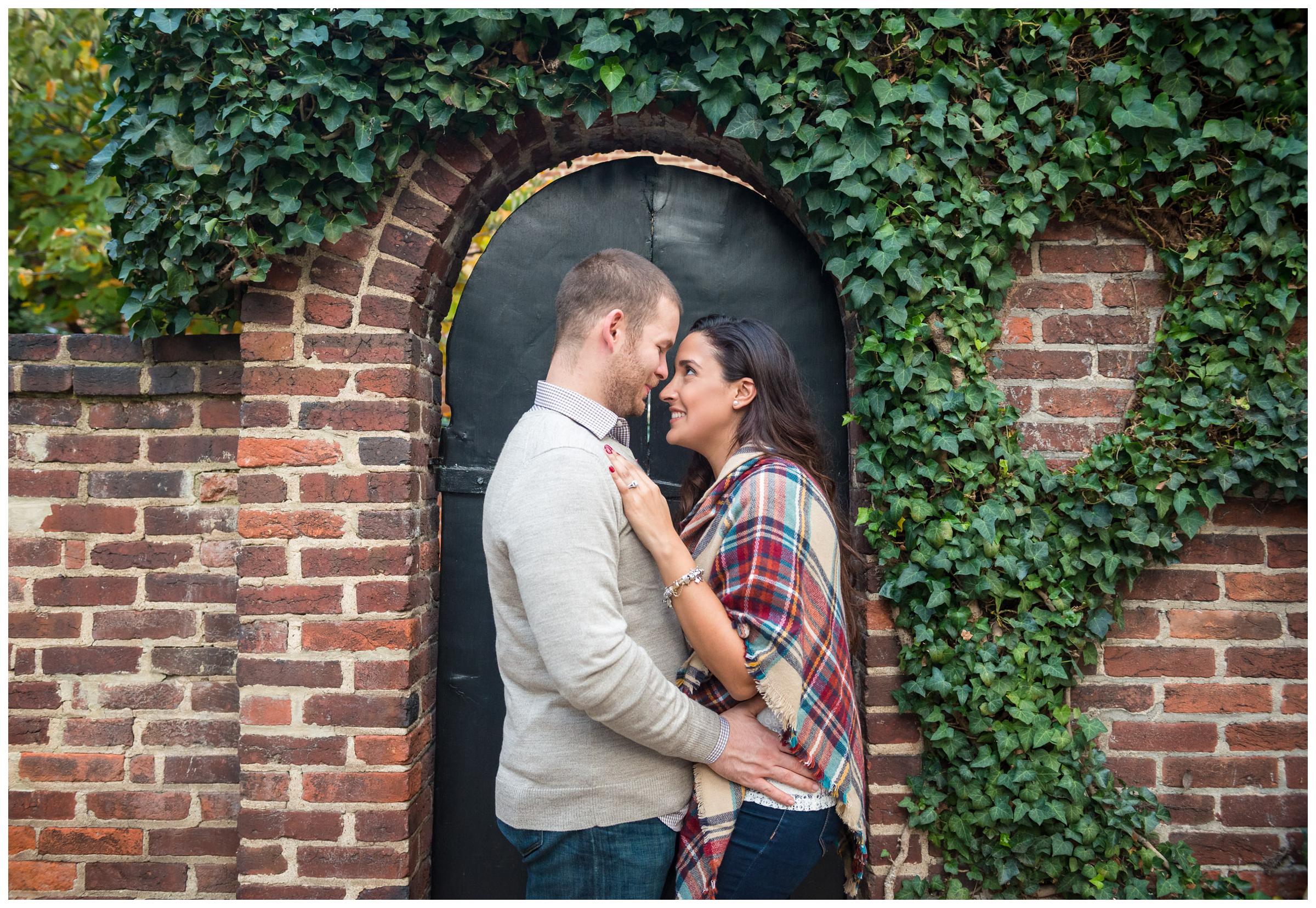 engaged couple in front of brick wall and archway surrounded by vines