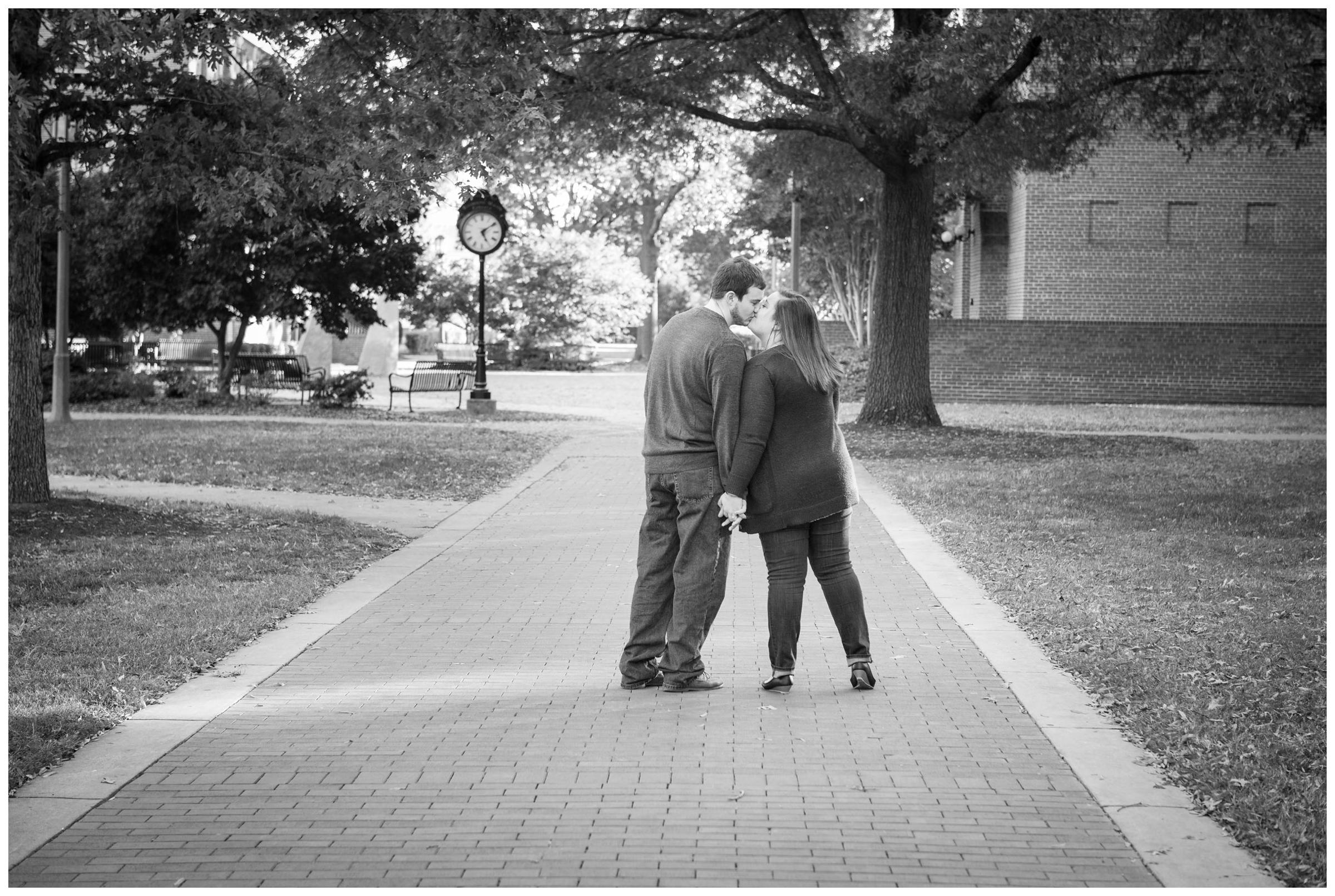 Engaged couple kissing near clock on Randolph-Macon campus in Ashland, Virginia.