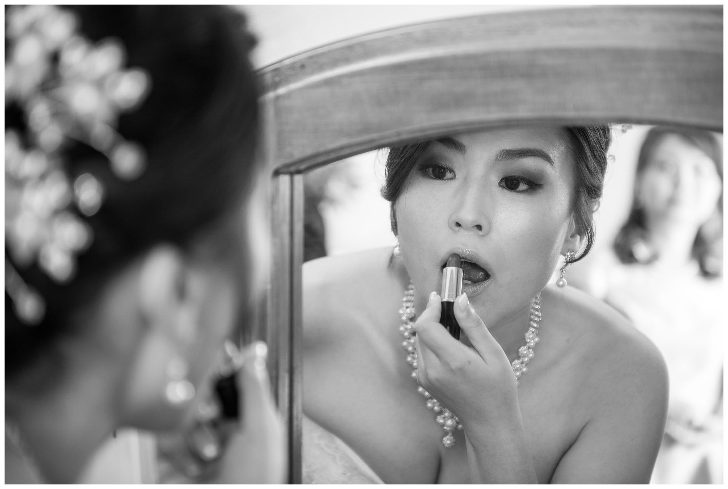 Bride applying lipstick in mirror before wedding ceremony.