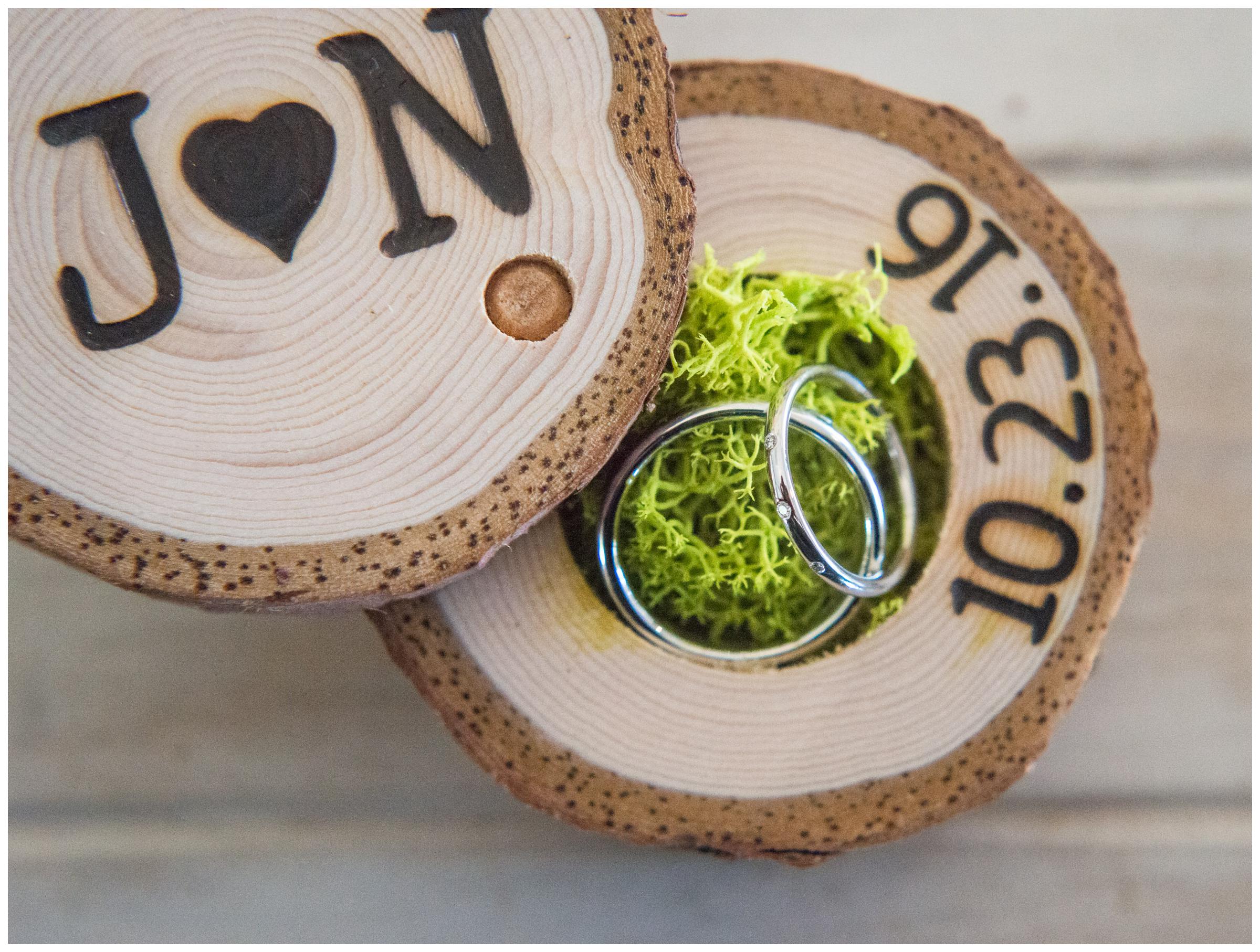 Rustic engraved wooden ring box with moss and wedding bands.