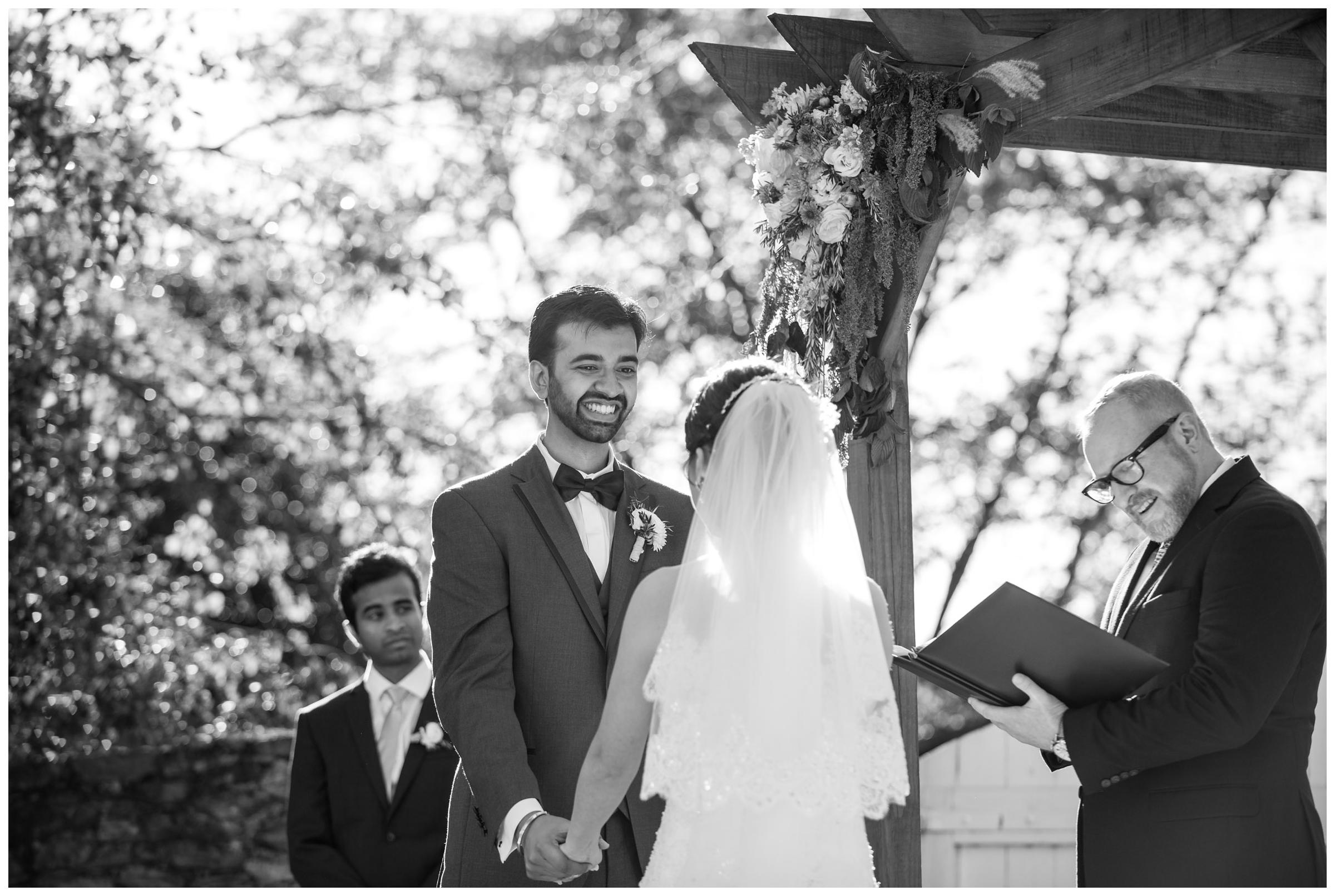 Groom smiling during rustic outdoor wedding ceremony.