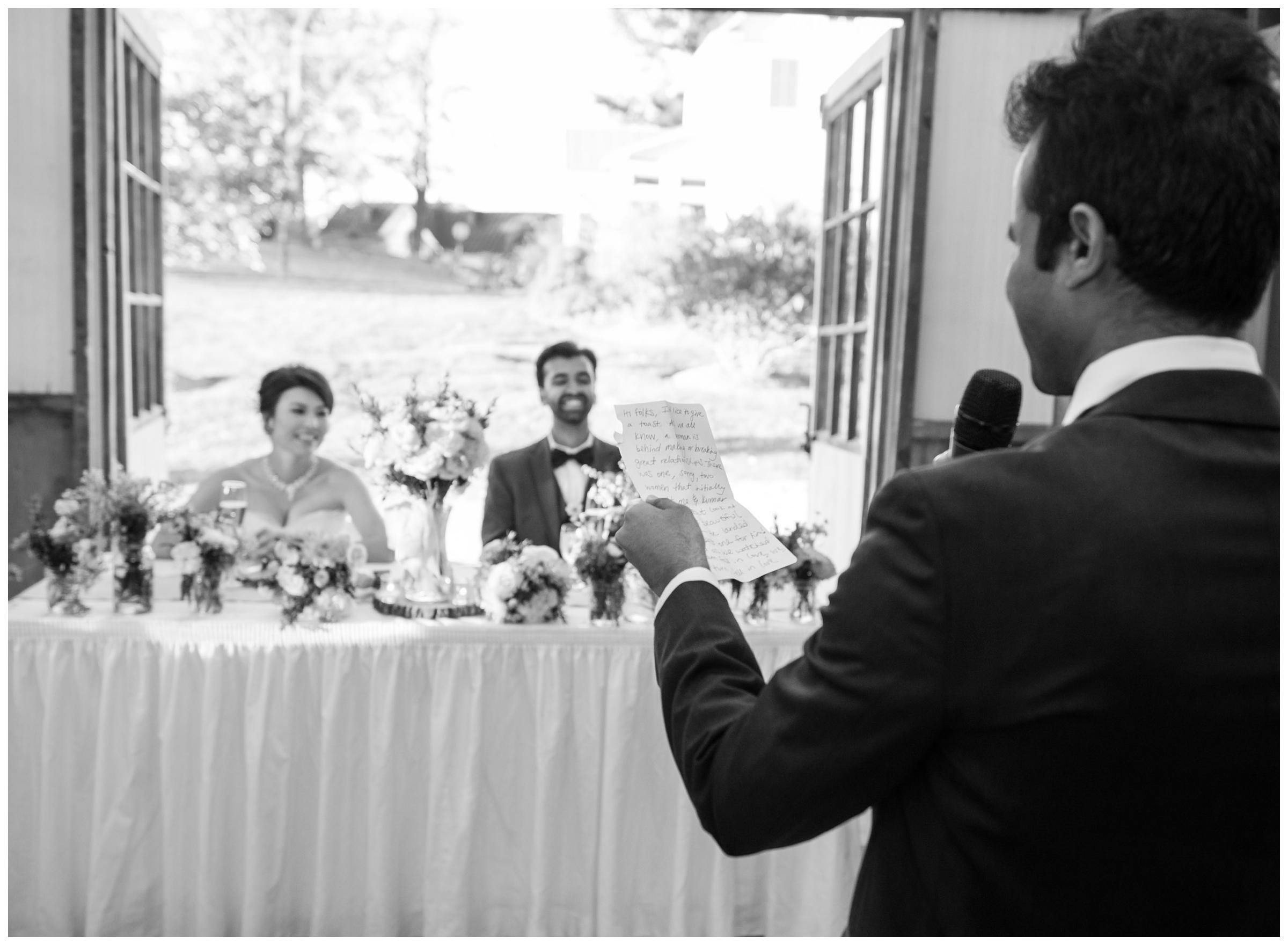 Groomsman gives toast during rustic barn wedding reception.