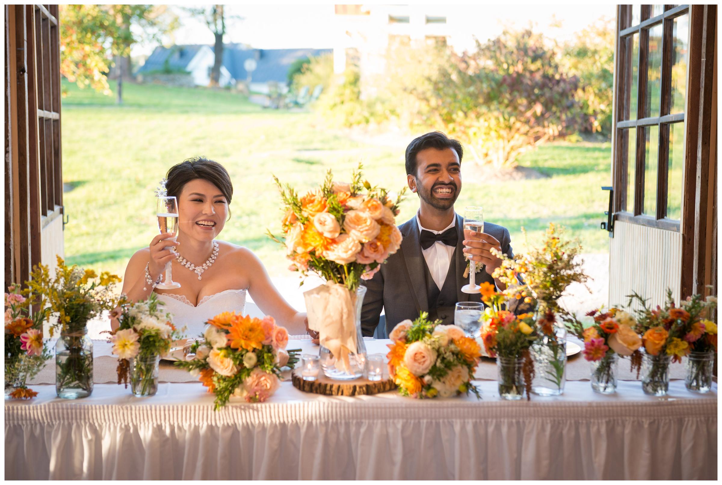 Bride and groom laugh during toasts at rustic barn wedding reception in Northern Virginia.