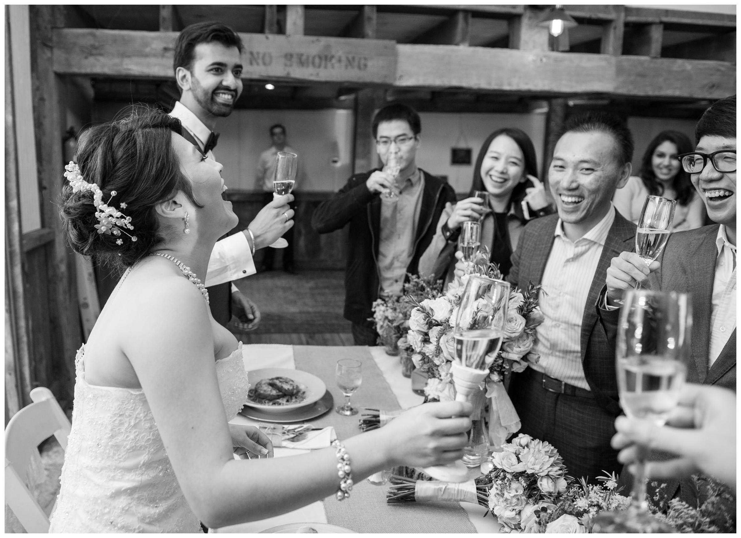 Newlyweds laugh with guests at rustic barn wedding.