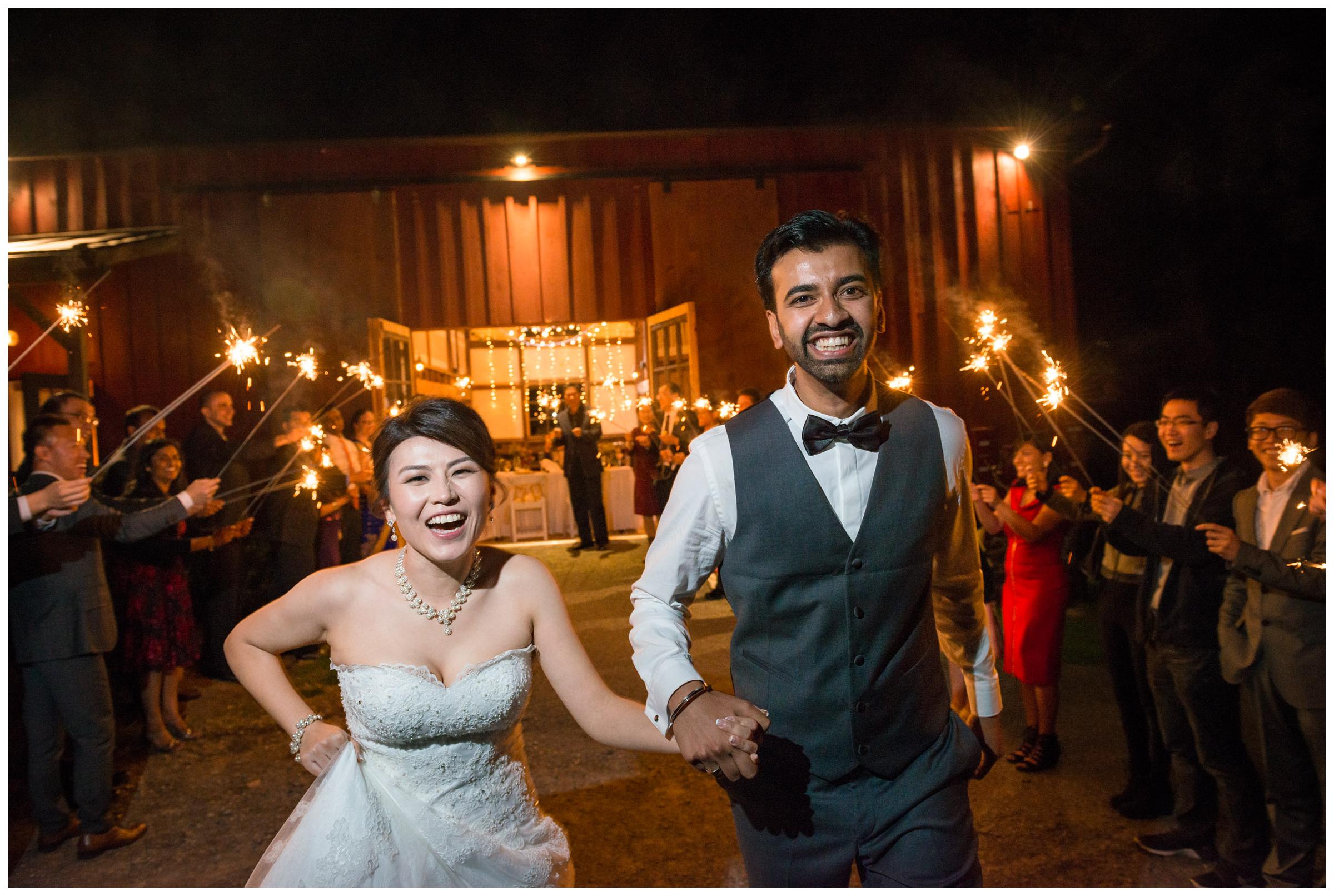 Bride and groom during sparkler wedding reception exit in rustic barn.