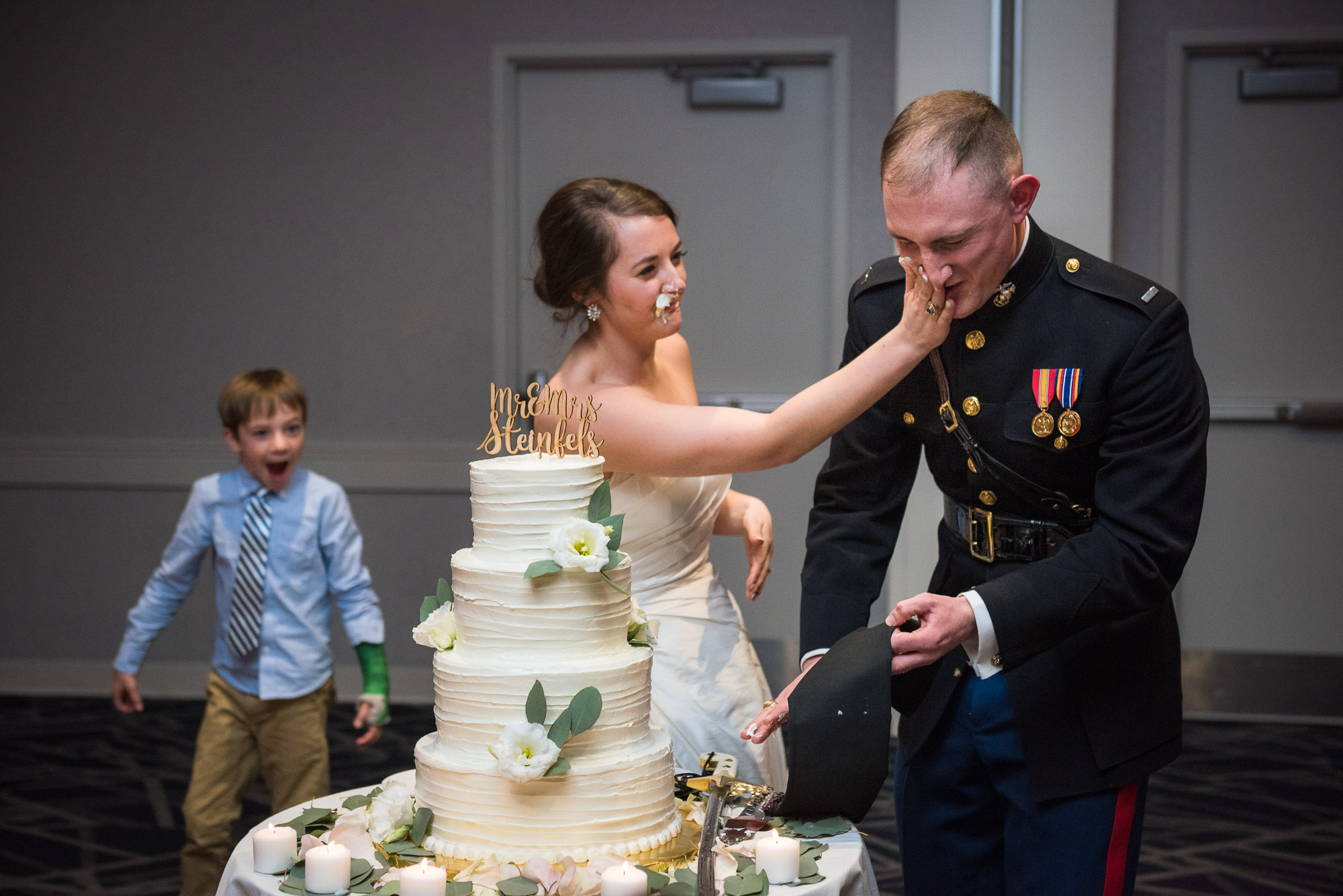 bride smashing cake into groom's face after Marine military sword cake cutting