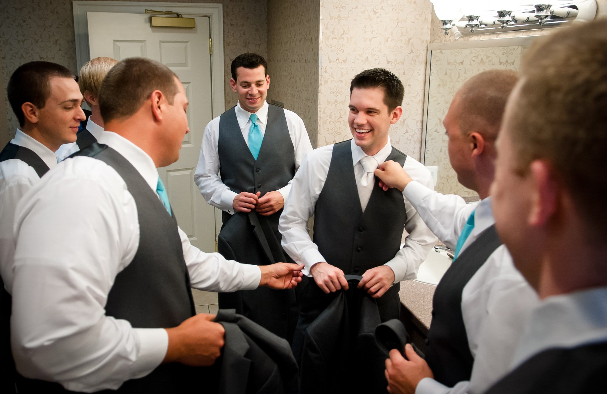groomsmen helping groom get dressed before wedding