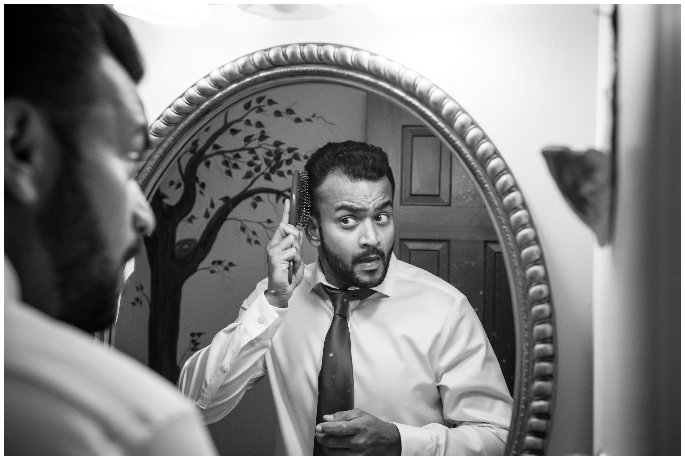 Indian wedding groom getting ready and combing hair in mirror