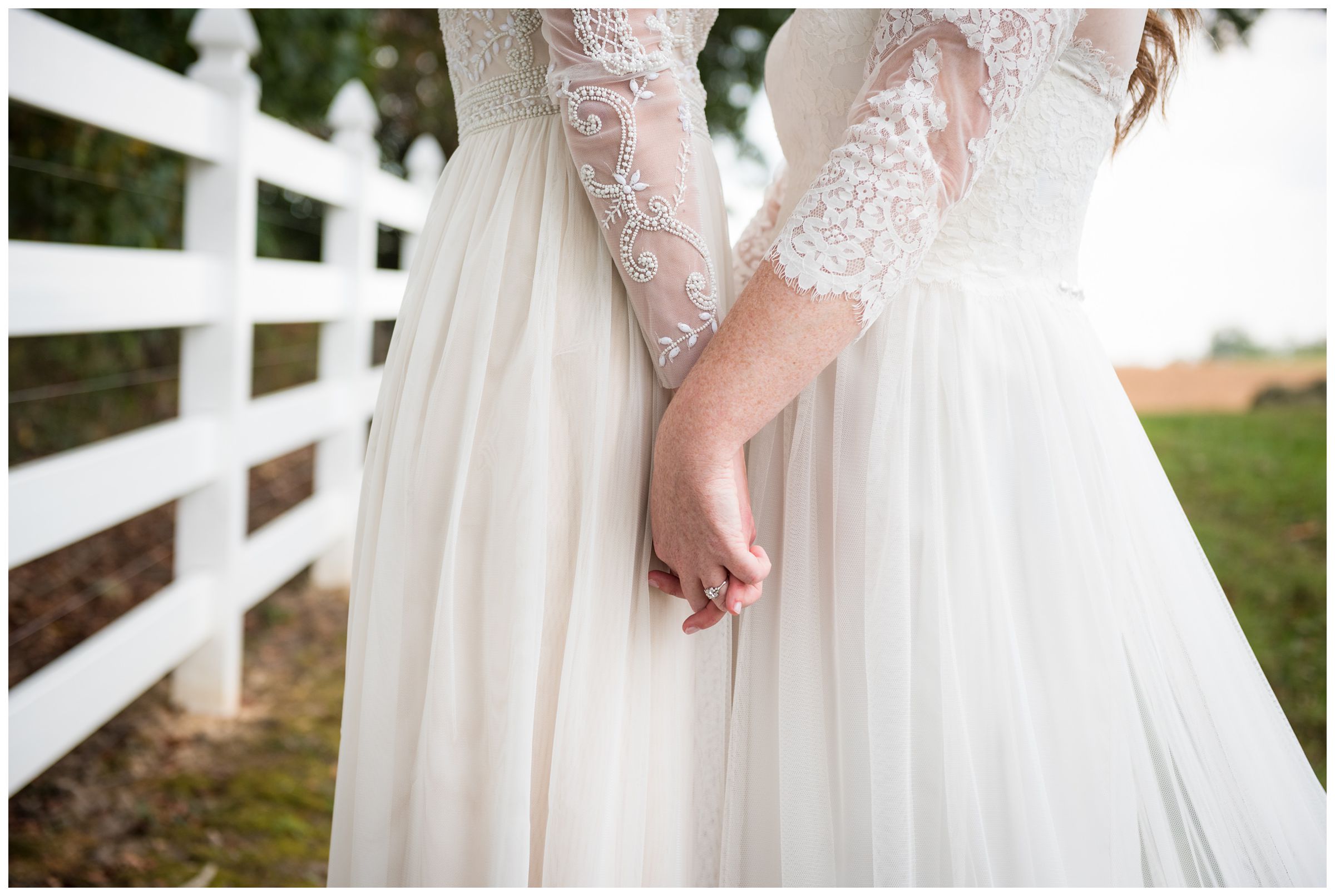 Two brides holding hands on wedding day in dresses with lace sleeves.