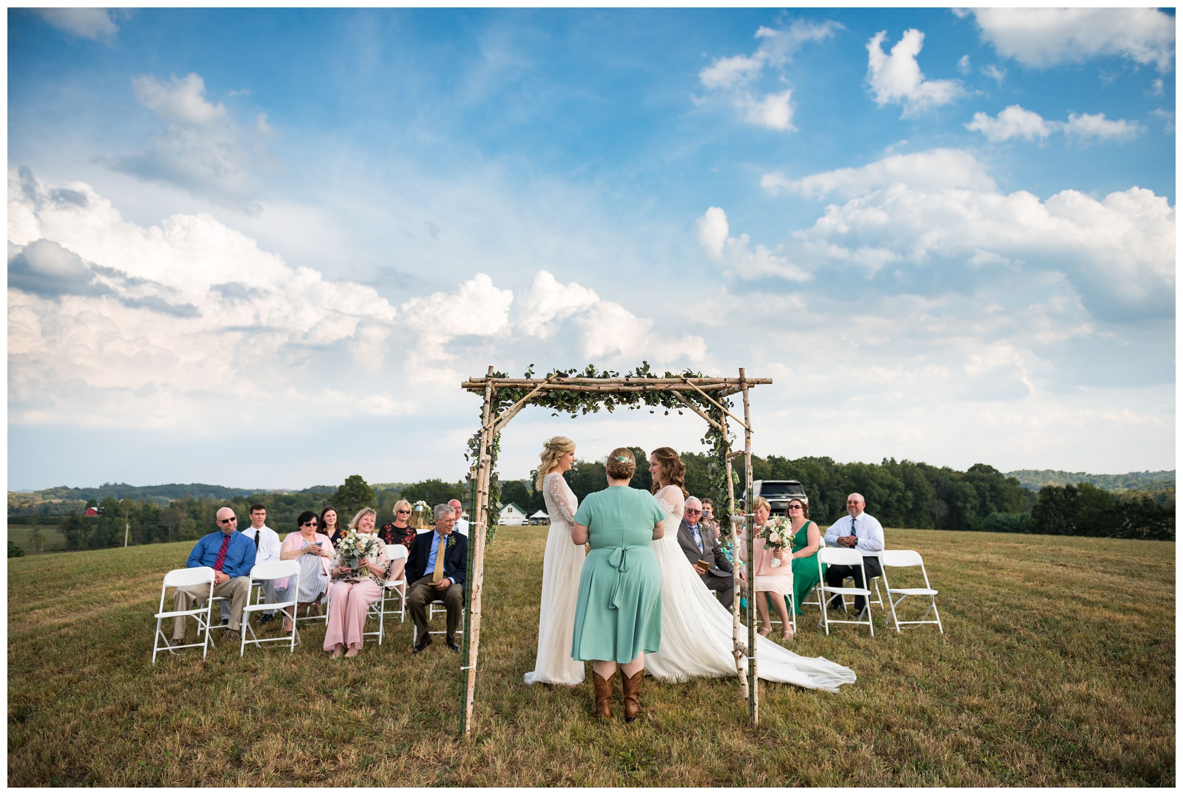 Intimate same-sex wedding ceremony with two brides on farm hilltop.