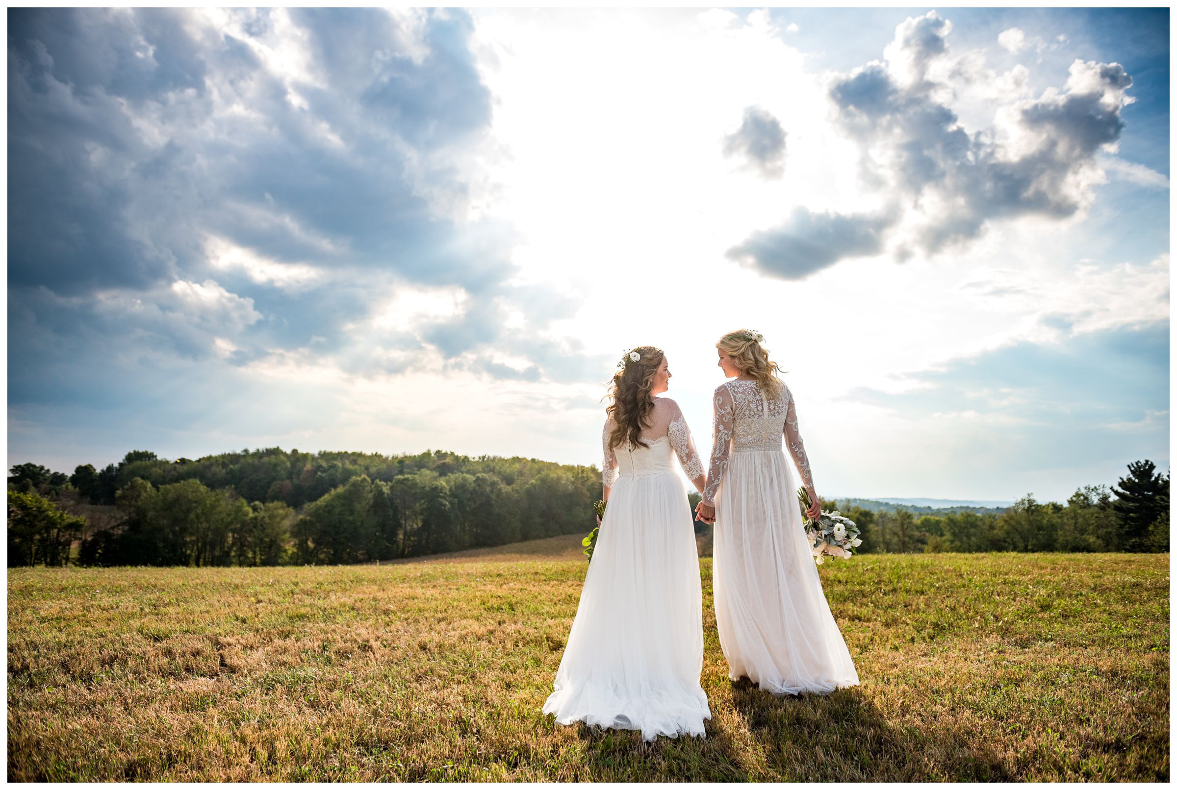 LGBTQ same-sex wedding portraits with two brides on hilltop after farm wedding ceremony.