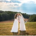 Two brides kissing on hilltop on wedding day